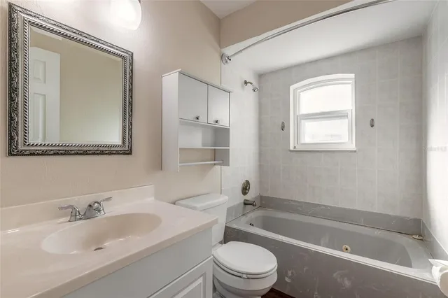 a bathroom with a bathtub shower sink vanity mirror and toilet