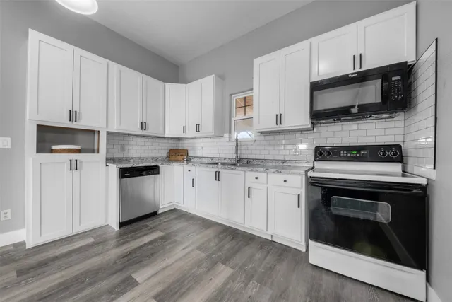 a kitchen with stainless steel appliances granite countertop a stove a microwave oven a sink dishwasher and white cabinets with wooden floor