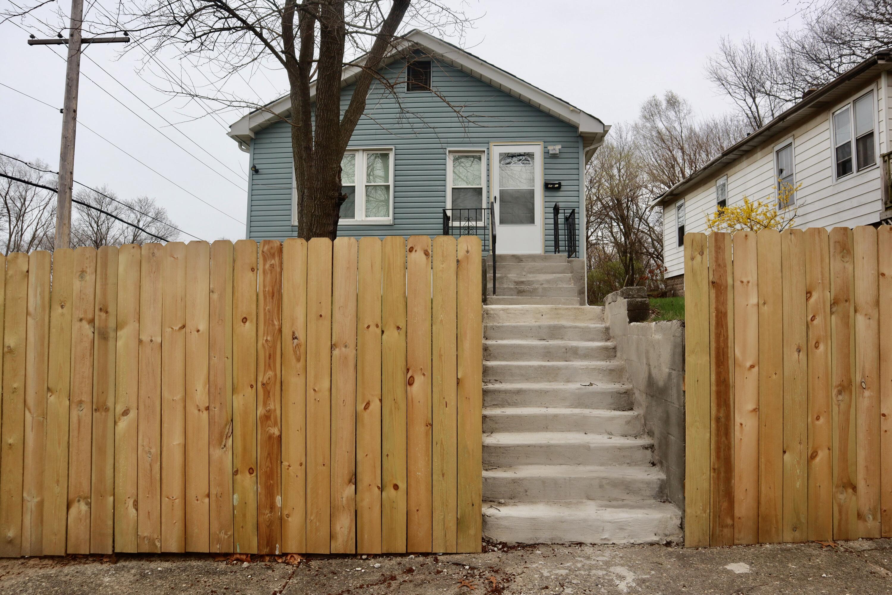 a view of a house with wooden fence next to a yard