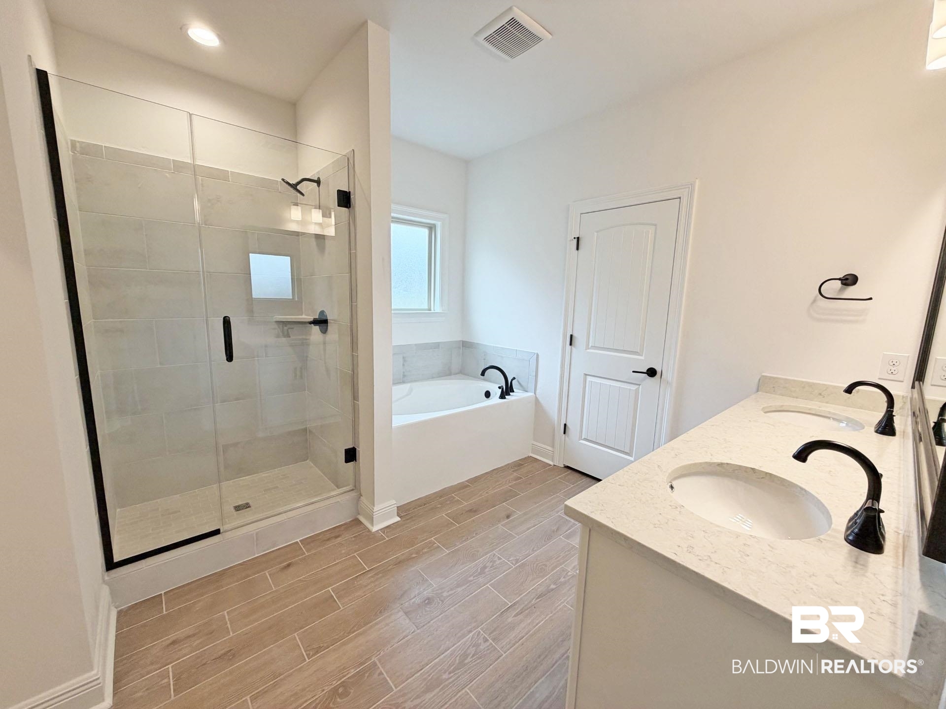 1753 Breckinridge Place Foley, AL 36535 - Photo 13 of 24 Bathroom featuring wood-finish tile flooring, a glass-enclosed shower with tile surround, a freestanding soaking tub, and a dual vanity with undermount sinks and dark bronze fixtures