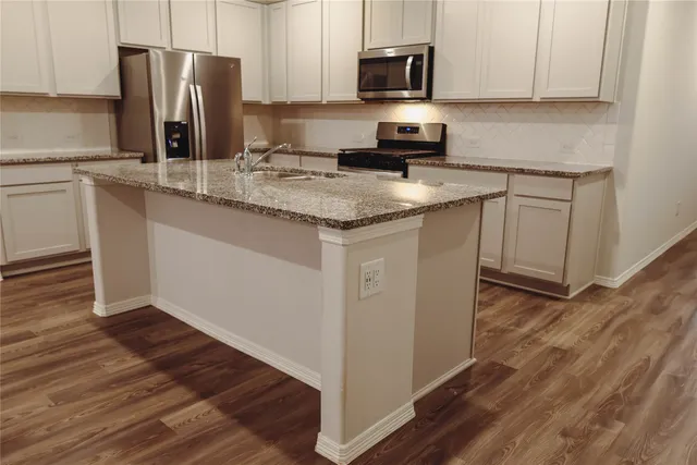 a kitchen with stainless steel appliances granite countertop a refrigerator a stove a sink and white cabinets with wooden floor