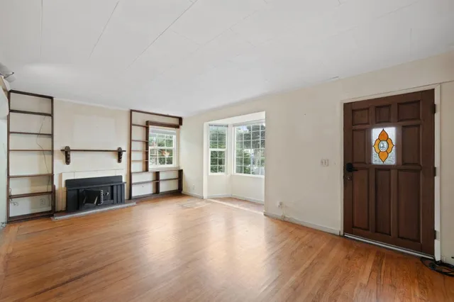 an empty room with wooden floor fireplace and windows