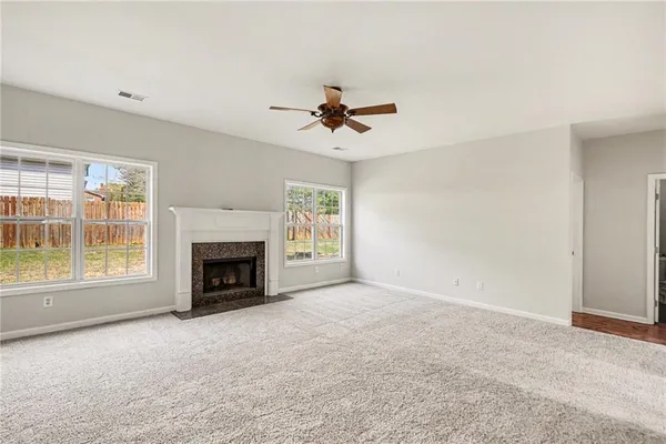 an empty room with windows fireplace and a ceiling fan