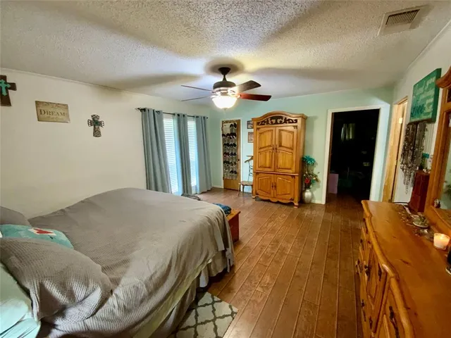 a bedroom with a bed ceiling fan and a wooden floor