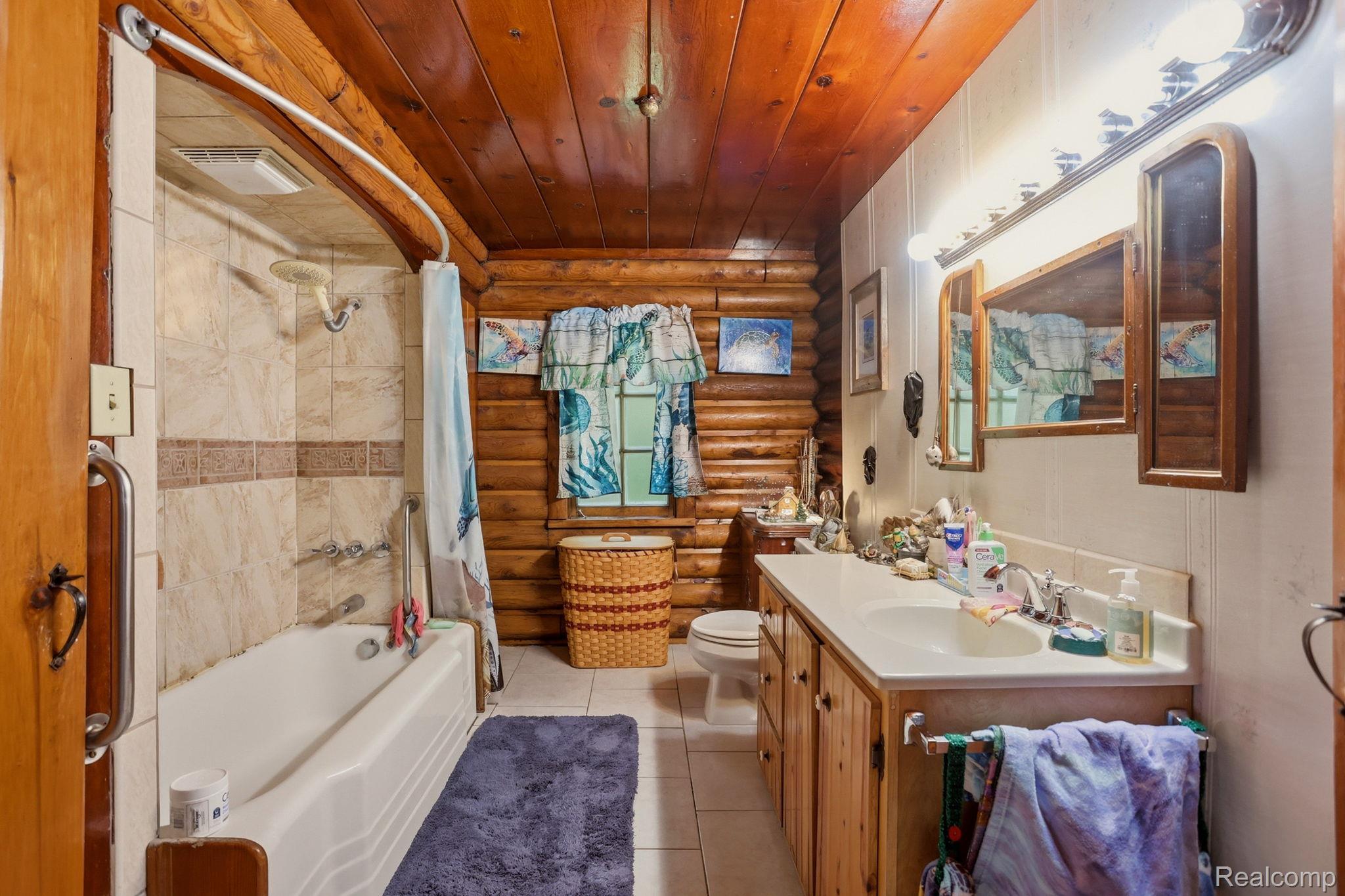 3814 South Towerline Road Bridgeport, MI 48722 - Photo 26 of 52 Bathroom featuring a log wall, a wood-paneled ceiling, a tiled shower-tub combination, and a double vanity with an integrated sink