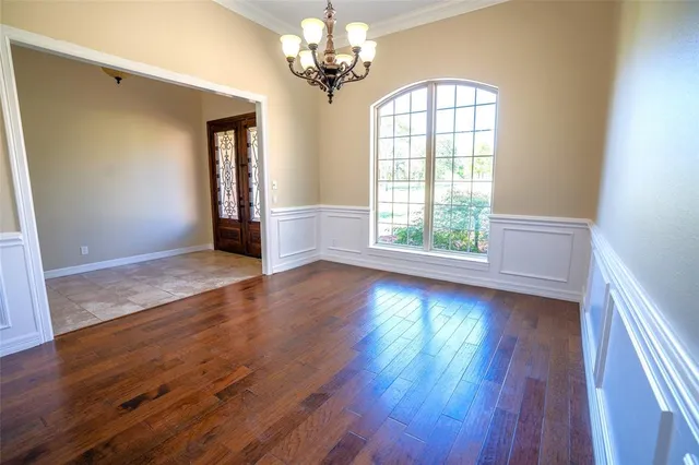 an empty room with wooden floor chandelier and windows