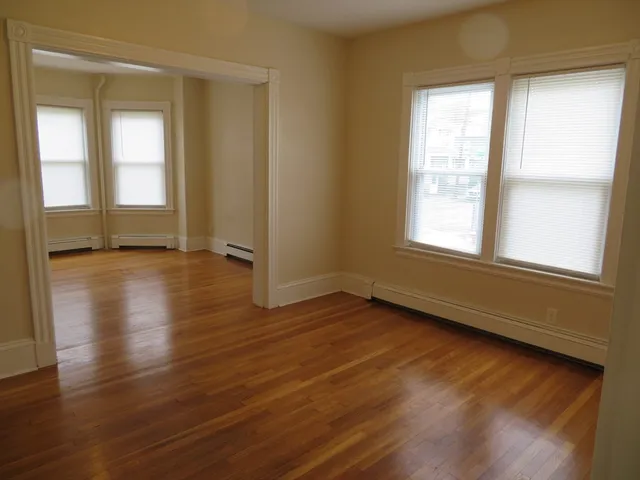 a view of an empty room with wooden floor and a window