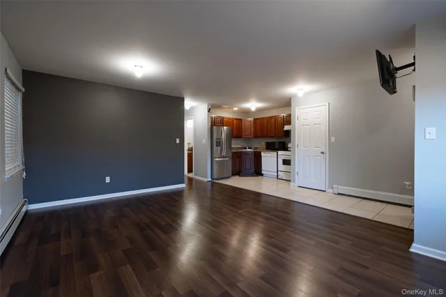 an empty room with wooden floor kitchen view and a window