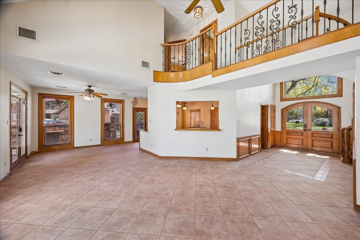 1835 Raintree Circle Seabrook, TX 77586 - Photo 50 of 50 This spacious living area features high ceilings and a loft with elegant iron railings. It has large windows and double wooden doors that bring in natural light, while the open floor plan seamlessly connects to a kitchen area with a pass-through. The tile flooring adds a clean, modern touch.