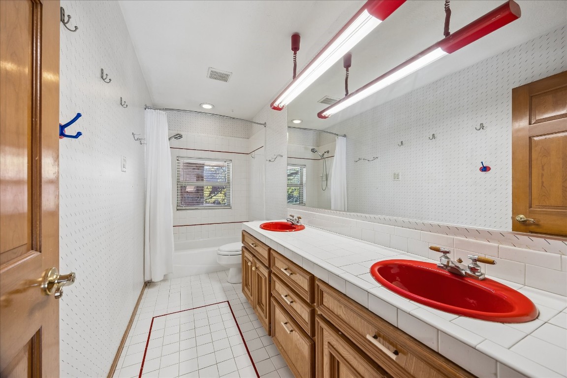 1835 Raintree Circle Seabrook, TX 77586 - Photo 24 of 50 This bathroom features a double vanity with striking red sinks, ample counter space, and wooden cabinetry. It includes a bathtub with a shower and a large mirror, all set against a clean white tile backdrop with subtle accents. Natural light enters through a window, enhancing the bright atmosphere.