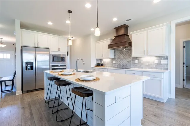 a kitchen with stainless steel appliances granite countertop a sink a stove a refrigerator and island with wooden floor