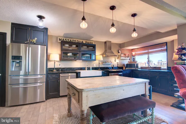 a room with stainless steel appliances kitchen island granite countertop a refrigerator a stove a sink and a dining table with wooden floor