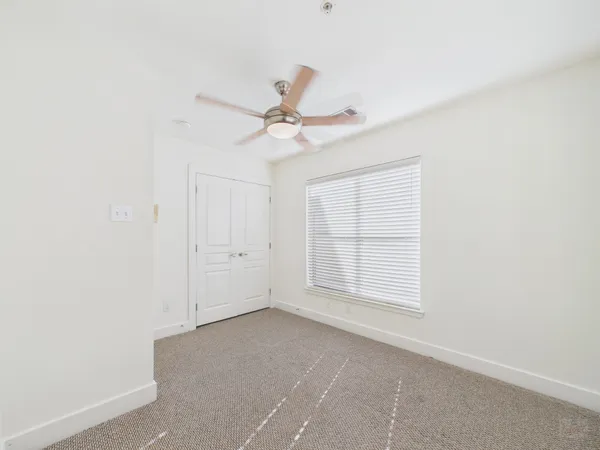 an empty room with chandelier fan and windows