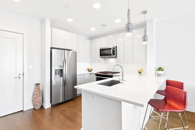 a kitchen with stainless steel appliances a stove a refrigerator a sink a microwave a dining table and chairs with wooden floor