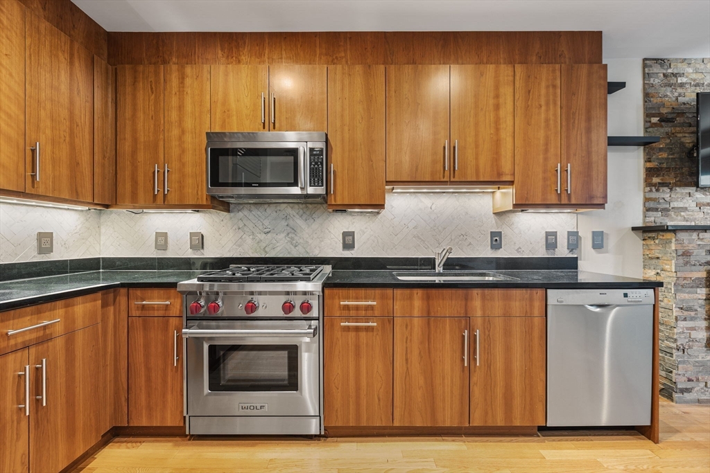 80 Broad Street, Unit 805 Boston, MA 02110 - Photo 10 of 22 a kitchen with granite countertop wood cabinets stainless steel appliances and sink