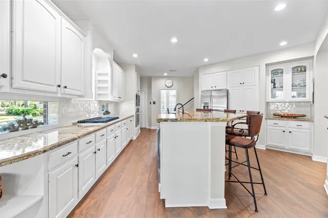 a kitchen with stainless steel appliances kitchen island granite countertop a stove a sink and white cabinets with wooden floor