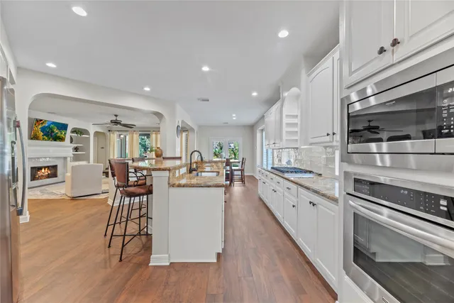 a kitchen with stainless steel appliances granite countertop a stove top oven a sink a dining table and chairs with wooden floor