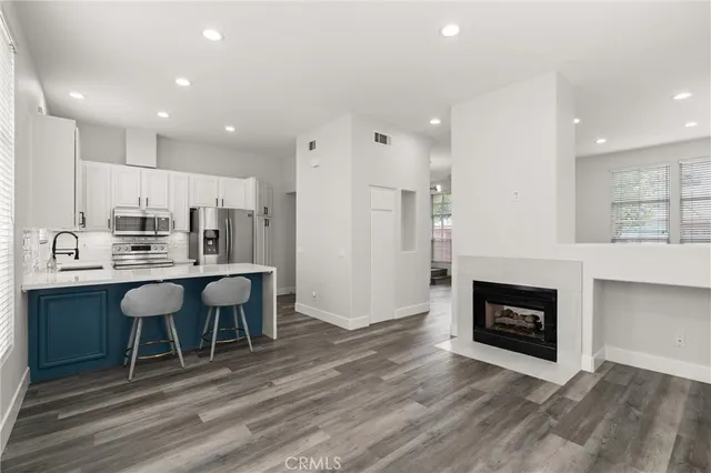 a living room with stainless steel appliances furniture a fireplace a flat screen tv and view kitchen