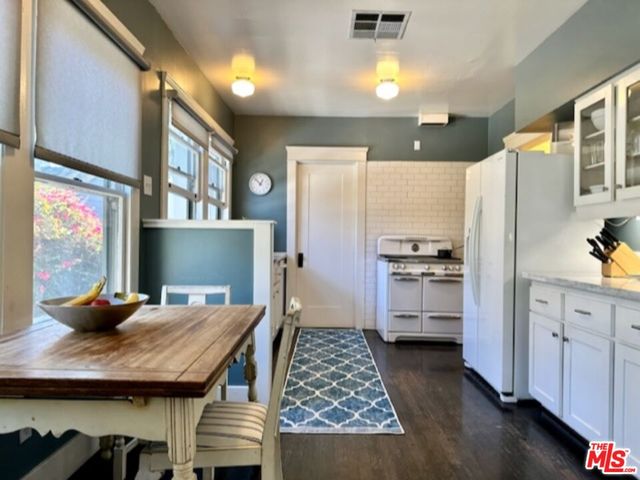 a kitchen with stainless steel appliances kitchen island granite countertop a refrigerator a stove and white cabinets with wooden floor