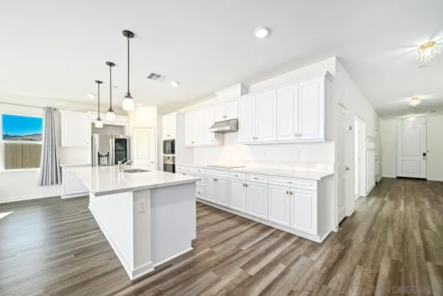 a large kitchen with kitchen island a large counter top a sink a stove and a chandelier