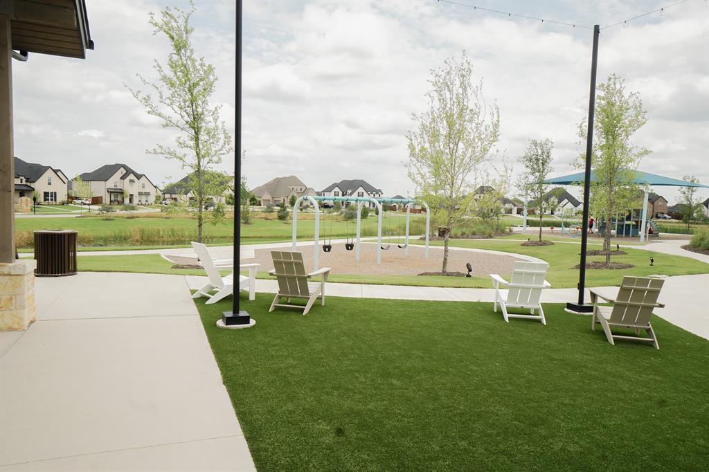 1309 Old Rocksprings Pass Mansfield, TX 76063 - Photo 35 of 36 Expansive outdoor area featuring a manicured artificial turf lawn with Adirondack chairs, a playground with swings, and mature trees, bordered by a concrete pathway