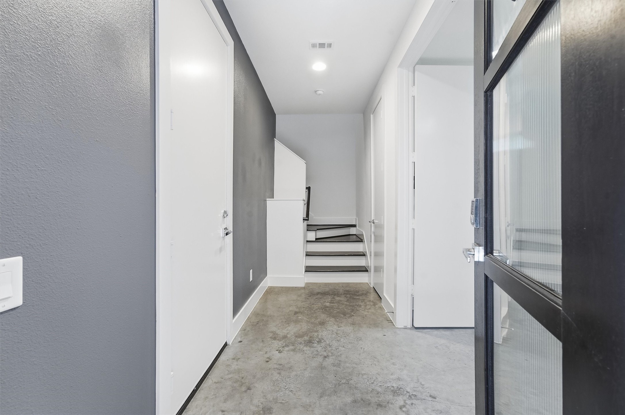 2338 Commerce Street Houston, TX 77003 - Photo 7 of 29 The first floor entryway features a modern design with gray walls, sleek concrete flooring, and has access to bottom level bedroom with en-suite bath. The space is brightened by recessed lighting and offers a clean, minimalist aesthetic. Garage door located on your left.
