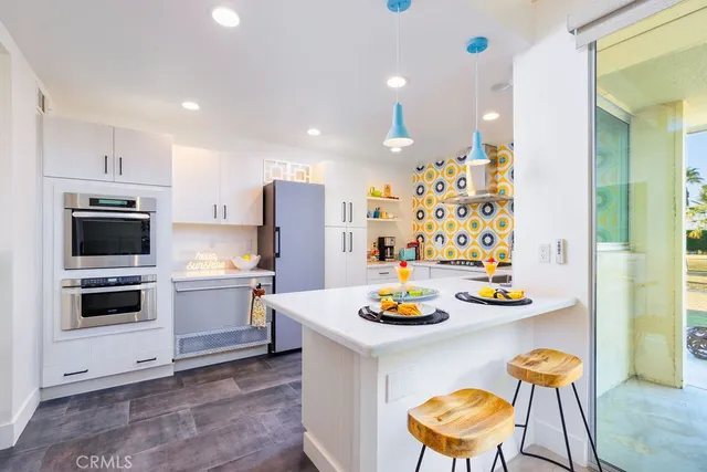 a kitchen with stainless steel appliances a white refrigerator a stove a microwave oven a dining table and chairs with wooden floor