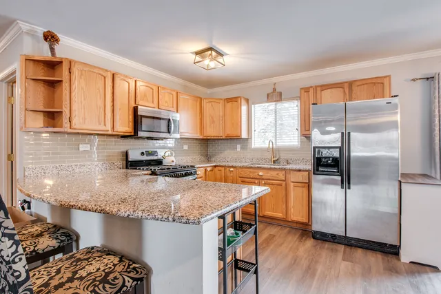 a kitchen with stainless steel appliances granite countertop a refrigerator a sink dishwasher a stove and white countertops with wooden floor