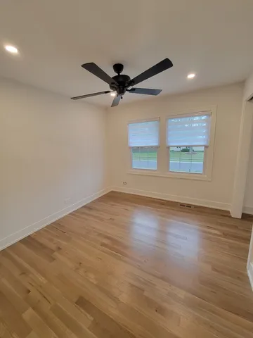 an empty room with wooden floor fan and windows