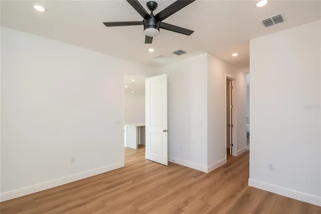 a view of an empty room with wooden floor and a ceiling fan