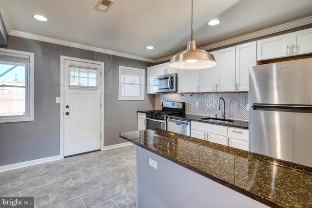 a kitchen with stainless steel appliances granite countertop a refrigerator a sink dishwasher a stove and white cabinets with wooden floor