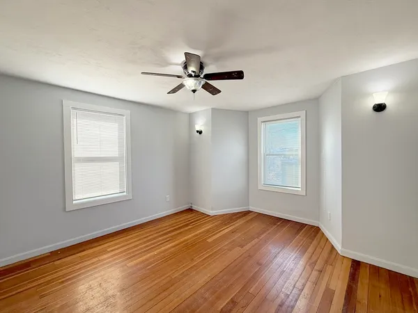 a view of empty room with wooden floor and fan