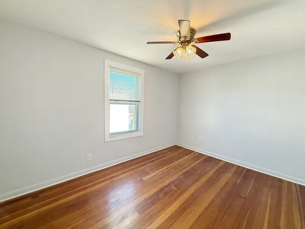 an empty room with wooden floor fan and windows