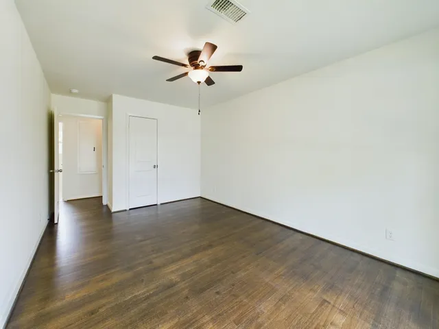 an empty room with wooden floor fan and windows