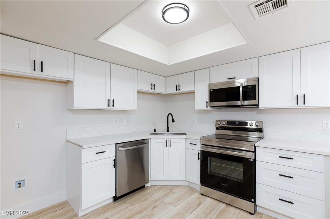 5905 Smoke Ranch Road, Unit A Las Vegas, NV 89108 - Photo 13 of 31 Kitchen featuring appliances with stainless steel finishes, white cabinets, light wood-style floors, and light stone countertops