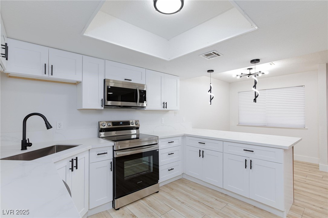 5905 Smoke Ranch Road, Unit A Las Vegas, NV 89108 - Photo 14 of 31 Kitchen with appliances with stainless steel finishes, white cabinets, light stone countertops, decorative light fixtures, and a peninsula