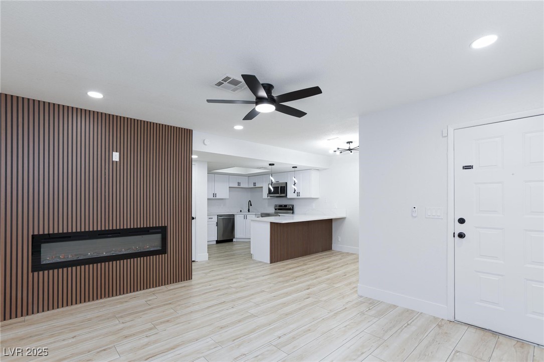 5905 Smoke Ranch Road, Unit A Las Vegas, NV 89108 - Photo 4 of 31 Kitchen with white cabinetry, a glass covered fireplace, a peninsula, recessed lighting, and light wood finished floors