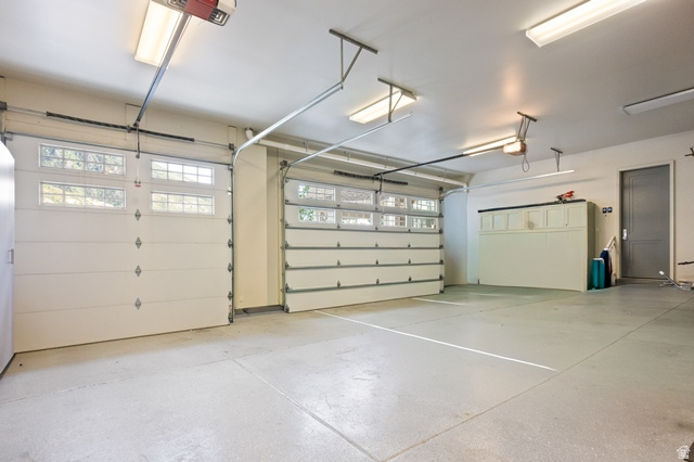 3 Carriagewood Cove, Unit 1088 Sandy, UT 84092 - Photo 63 of 79 Three-car garage featuring white sectional doors with upper-panel windows, exposed overhead garage door openers, painted concrete flooring, and built-in white cabinetry