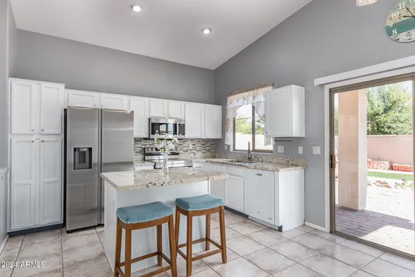 a kitchen with granite countertop white cabinets white appliances a large window and a sink