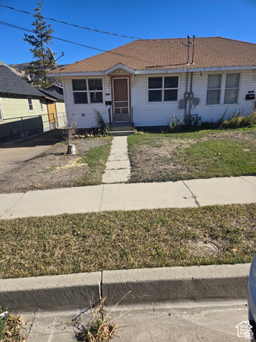 55 Bryner Street Helper, UT 84526 - Photo 2 of 8 White siding exterior with a brown shingle roof, featuring a front entry with a screen door and an established sidewalk