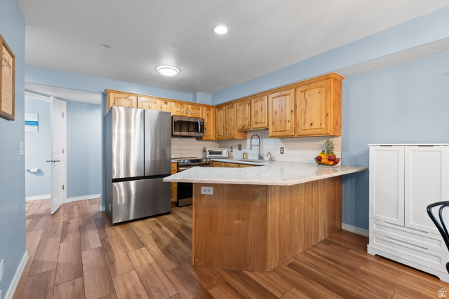 1625 Pages Pl Drive Bountiful, UT 84010 - Photo 8 of 31 Kitchen featuring stainless steel appliances, tasteful backsplash, light stone counters, a peninsula, and ceramic wood tile flooring