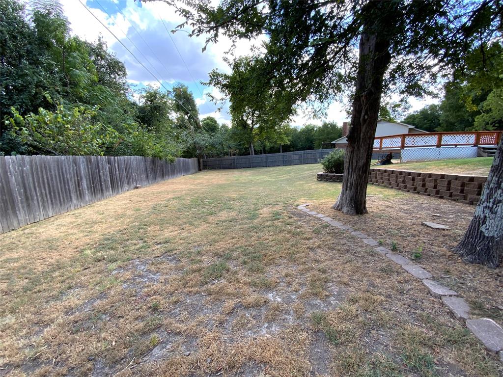 2020 Arbor Bend Road Bonham, TX 75418 - Photo 27 of 30 Expansive yard featuring mature trees, a wood privacy fence, and a retaining wall