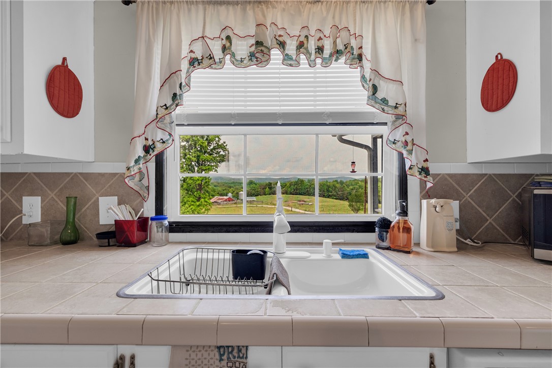 721 Cedar Crest Trail Walhalla, SC 29691 - Photo 11 of 47 A classic kitchen sink with tiled counters offers sweeping views of verdant hills and distant pastoral landscapes.