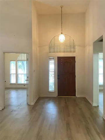 an empty room with wooden floor chandelier and windows