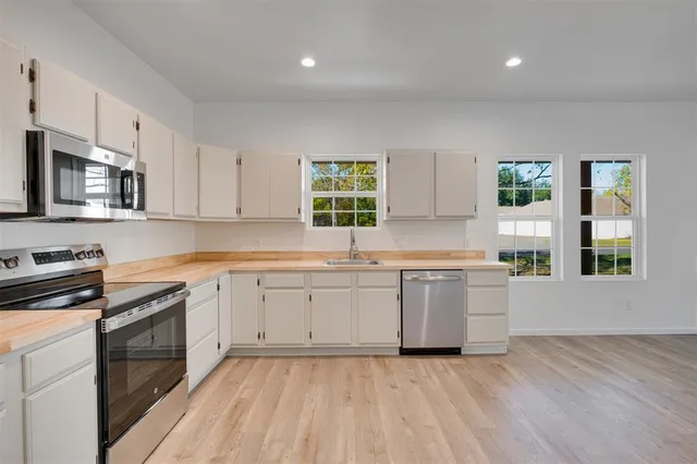 a kitchen with stainless steel appliances granite countertop a stove a sink dishwasher and a microwave oven with white cabinets