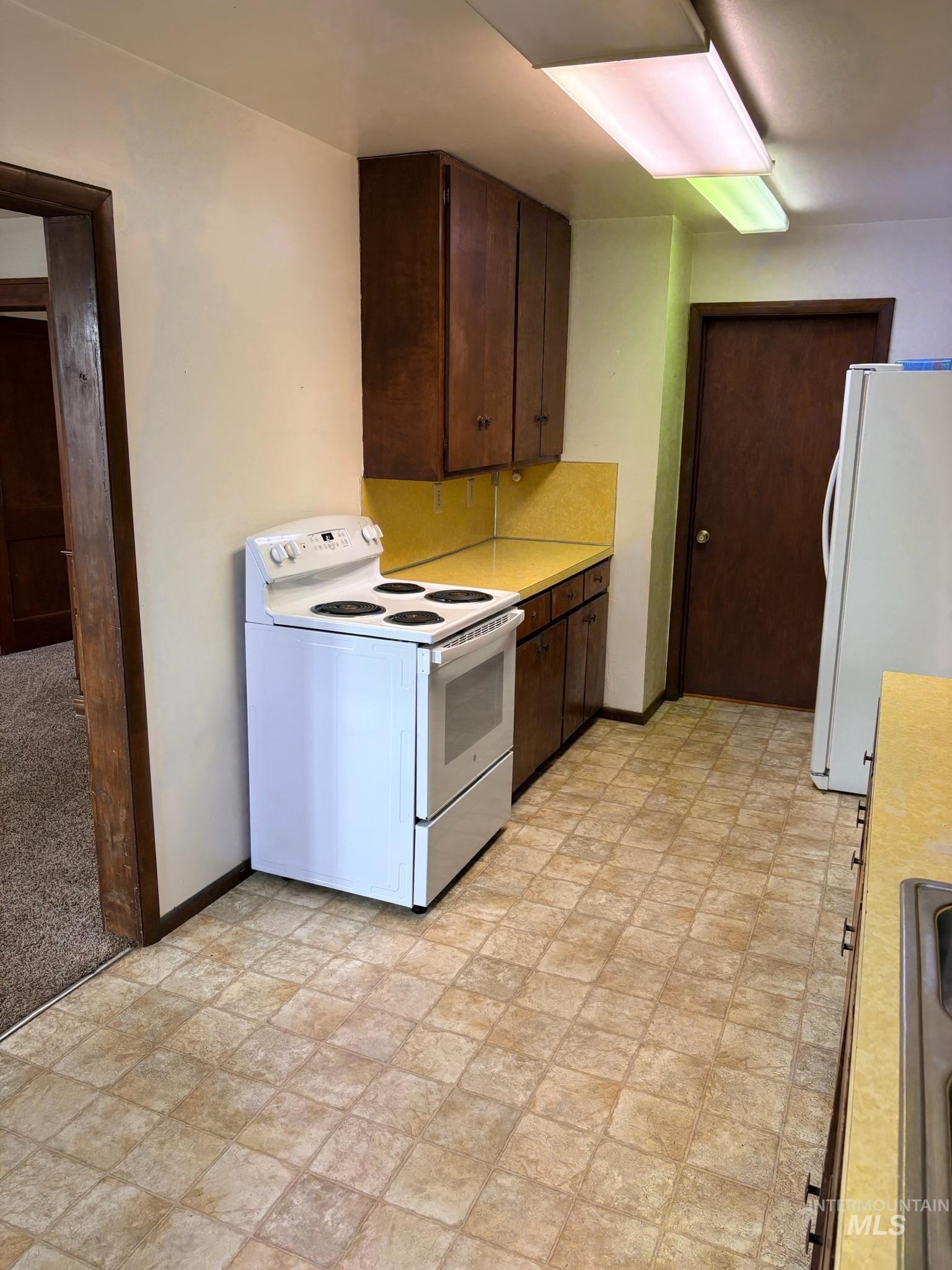 627 Southwest 3rd Street Fruitland, ID 83619 - Photo 14 of 35 Kitchen featuring white appliances, light countertops, dark brown cabinets, and stone finish flooring