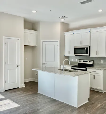 a kitchen with stainless steel appliances a stove a refrigerator a sink and white cabinets with wooden floor