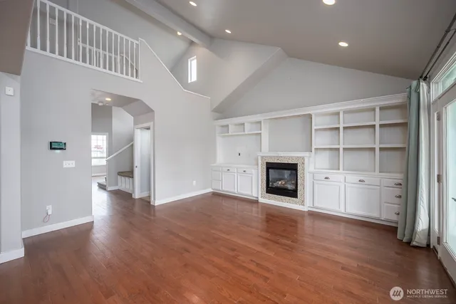 an empty room with wooden floor fireplace and windows