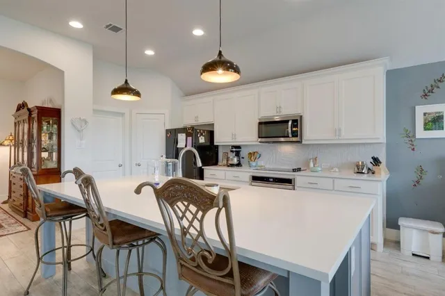 a kitchen with stainless steel appliances a stove a refrigerator a microwave oven a sink a dining table and chairs with wooden floor