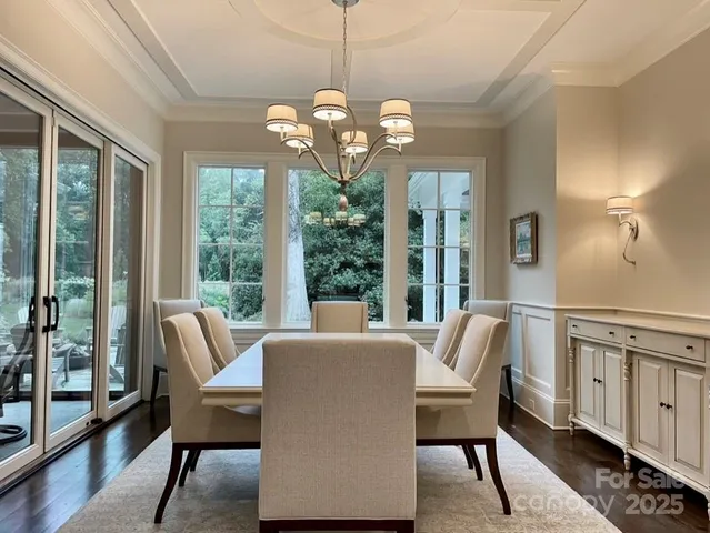a dining room with wooden floor a chandelier a flat screen tv and a large window